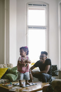 Smiling young man sitting by daughter standing on chess board at home