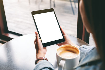 Cropped hand of woman holding digital tablet sitting at cafe