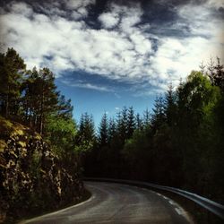 Road amidst trees against cloudy sky