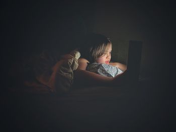 Rear view of girl using laptop on bed