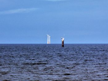 Lighthouse by sea against clear blue sky