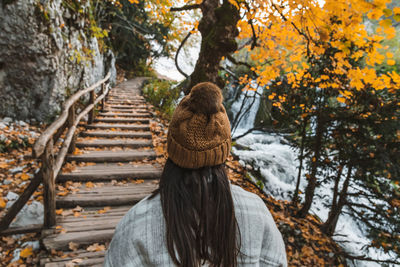 Rear view of young adult woman walking on wooden path in forest in autumn.