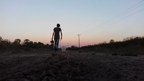 Rear view of man with dog walking on road standing against clear sky