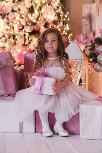 A beatiful girl with curly hair in white dress is holding of christmas box gift and sitting 