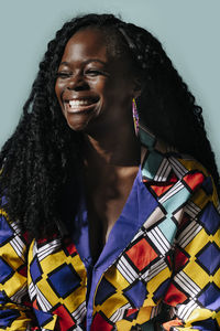 Happy african american woman with curly hair smiling and looking away while standing against blue background