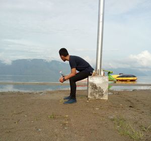 Side view full length of man sitting by pole at beach