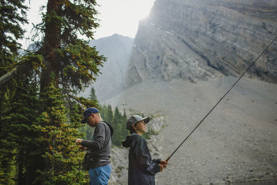 Side view of father and son fishing against mountains at forest