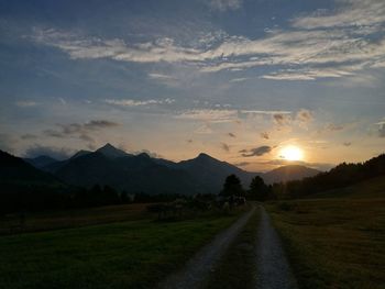 Empty road amidst field against sky during sunset