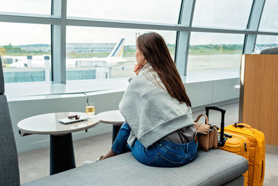 Young woman sitting in airport business lounge waiting for plane departure enjoying glass of  vine