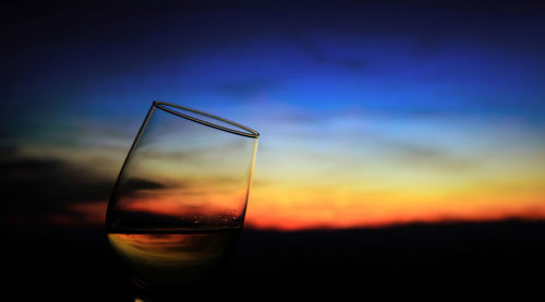 Close-up of wineglass against sky during sunset