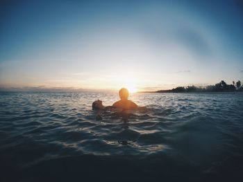 Back lit man carrying woman in sea against sky during sunset