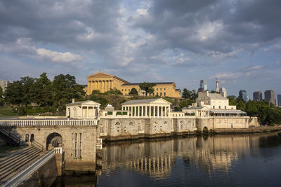 Arch bridge over river by buildings against sky