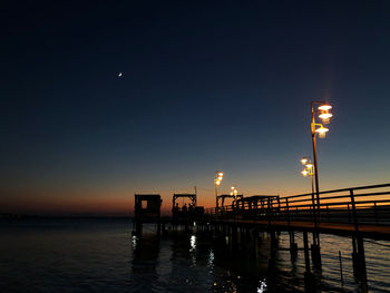 Illuminated pier over sea against sky at night