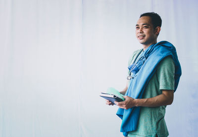 Young man using smart phone while standing against wall