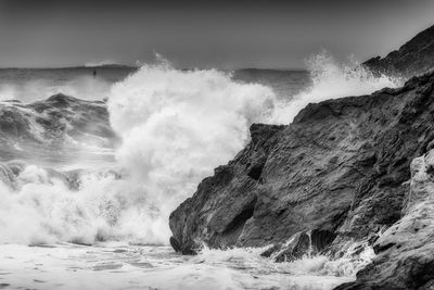 Waves splashing on rocks at shore against sky