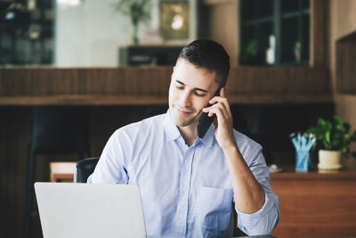 Businessman talking on phone while using laptop