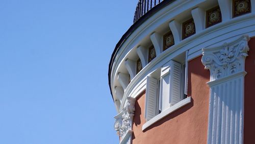 Low angle view of orange building with white shutter and ornamental  against clear blue sky