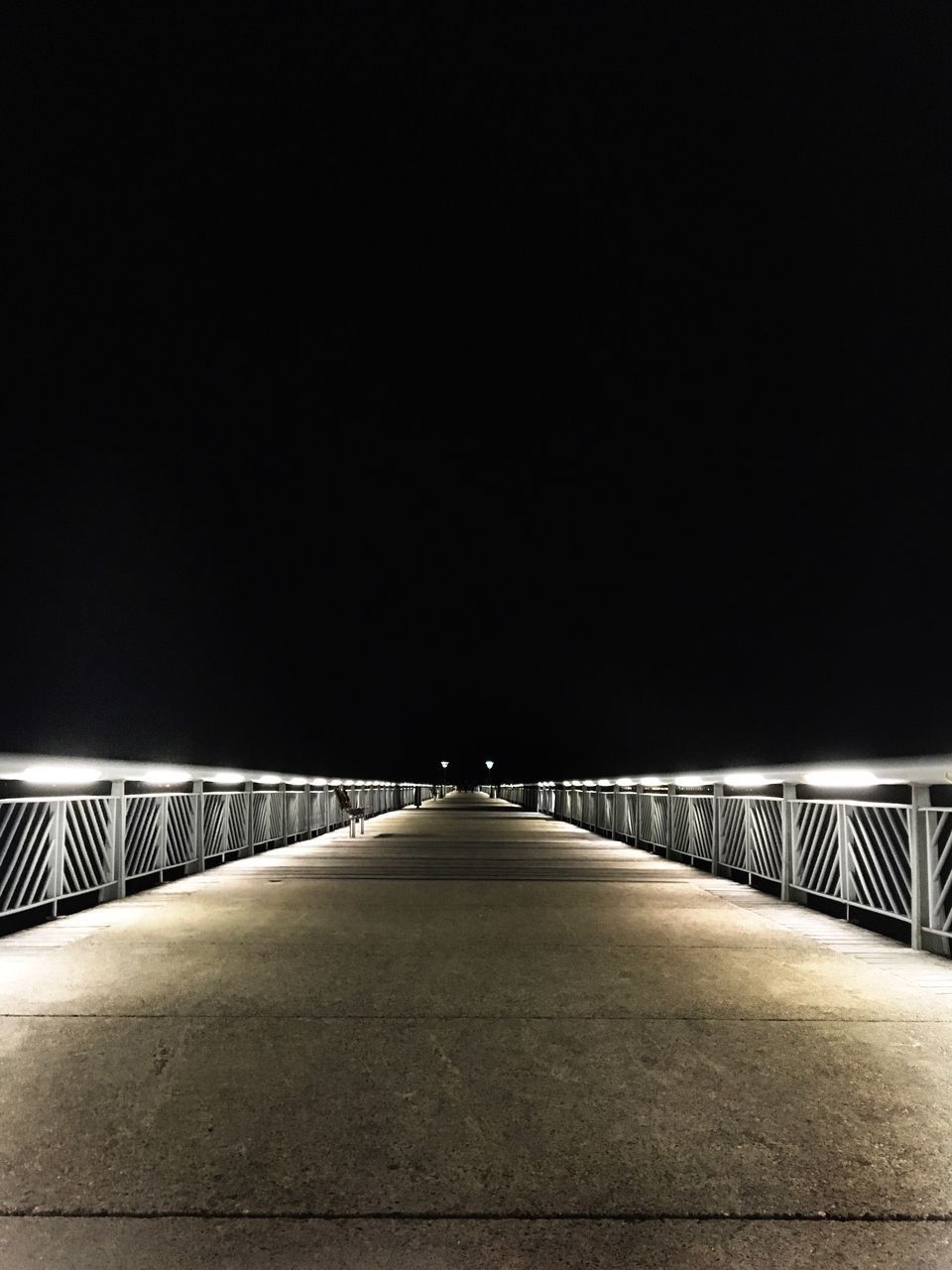 BRIDGE OVER ILLUMINATED ROAD AGAINST CLEAR SKY AT NIGHT