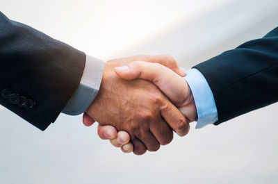 Cropped image of colleagues shaking hands against wall