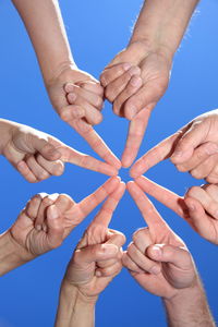 Cropped hand of people huddling against clear blue sky