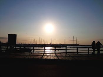 Silhouette people by railing against sky during sunset