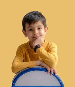 Portrait of cute girl looking away while sitting against yellow background