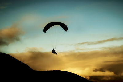 Low angle view of silhouette person paragliding against sky during sunset