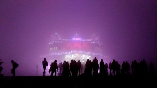 Silhouette people standing on illuminated street against sky at night