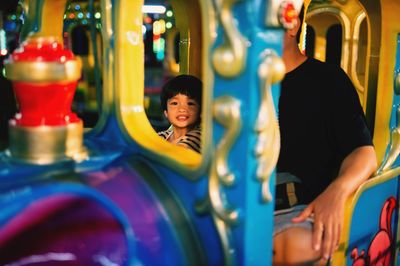 Portrait of boy sitting with father in amusement park ride at night