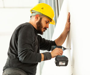 Worker screws plasterboard panels on an aluminum structure.