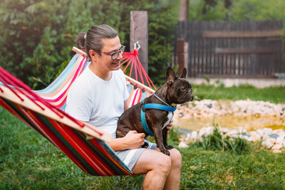 Man with french bulldog dog relaxing in hammock in the backyard