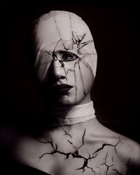 Close-up portrait of topless young woman face wrapped in bandage against black background