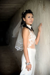 Thoughtful bride looking away while standing against wall