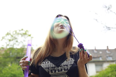 Young woman playing with bubbles while standing against sky