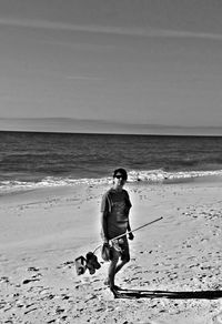 Young man in sunglasses with stick walking at beach during sunny day