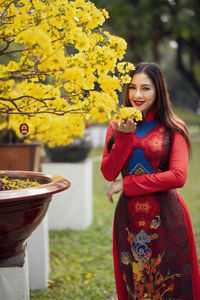 Portrait of smiling young woman standing by flowering plants