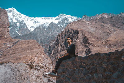 Portrait of young woman standing on rock against snowcapped mountains