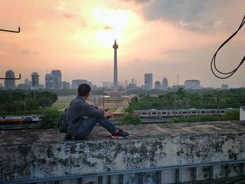 Man and buildings in city against sky during sunset