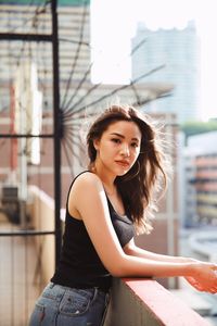 Portrait of young woman standing against buildings in city