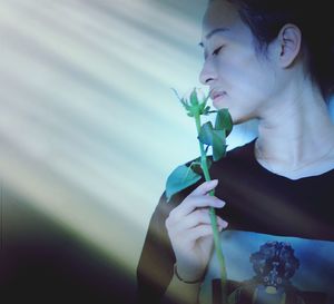 Young woman holding leaves against wall