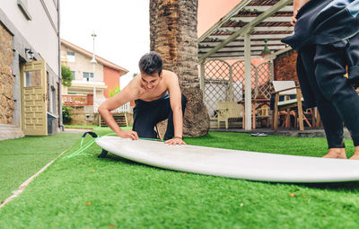 Young man cleaning surfboard while friend standing on lawn