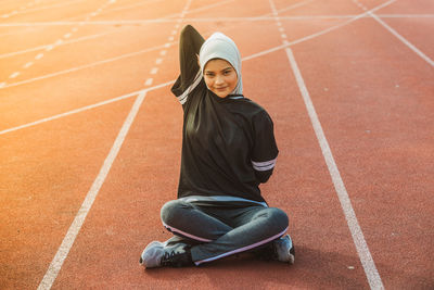 Portrait of female athlete stretching while sitting on track