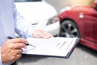 Midsection of customer signing document against cars