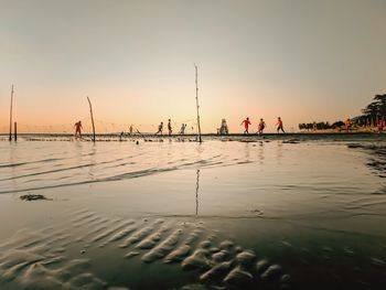 People on beach against sky during sunset