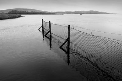 Wooden post by lake against sky