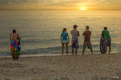 Rear view of people at beach during sunset