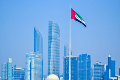 Low angle view of modern buildings against clear blue sky with uae flag