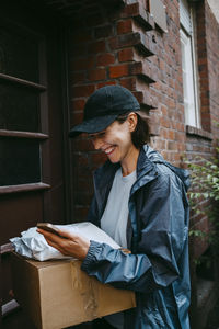 Happy female delivery person laughing while standing with parcel at doorstep