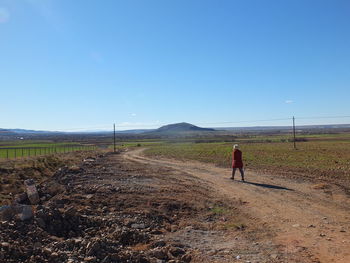 Rear view of woman walking on dirt road against clear sky