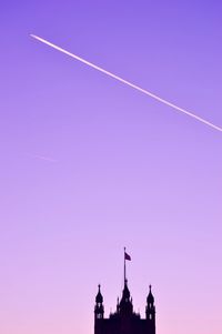 Low angle view of silhouette building against vapor trails in sky